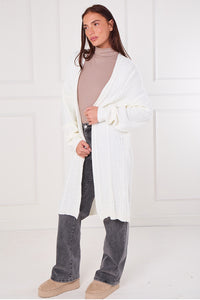 Woman wearing a white cardigan, beige turtleneck, and dark jeans against a white background