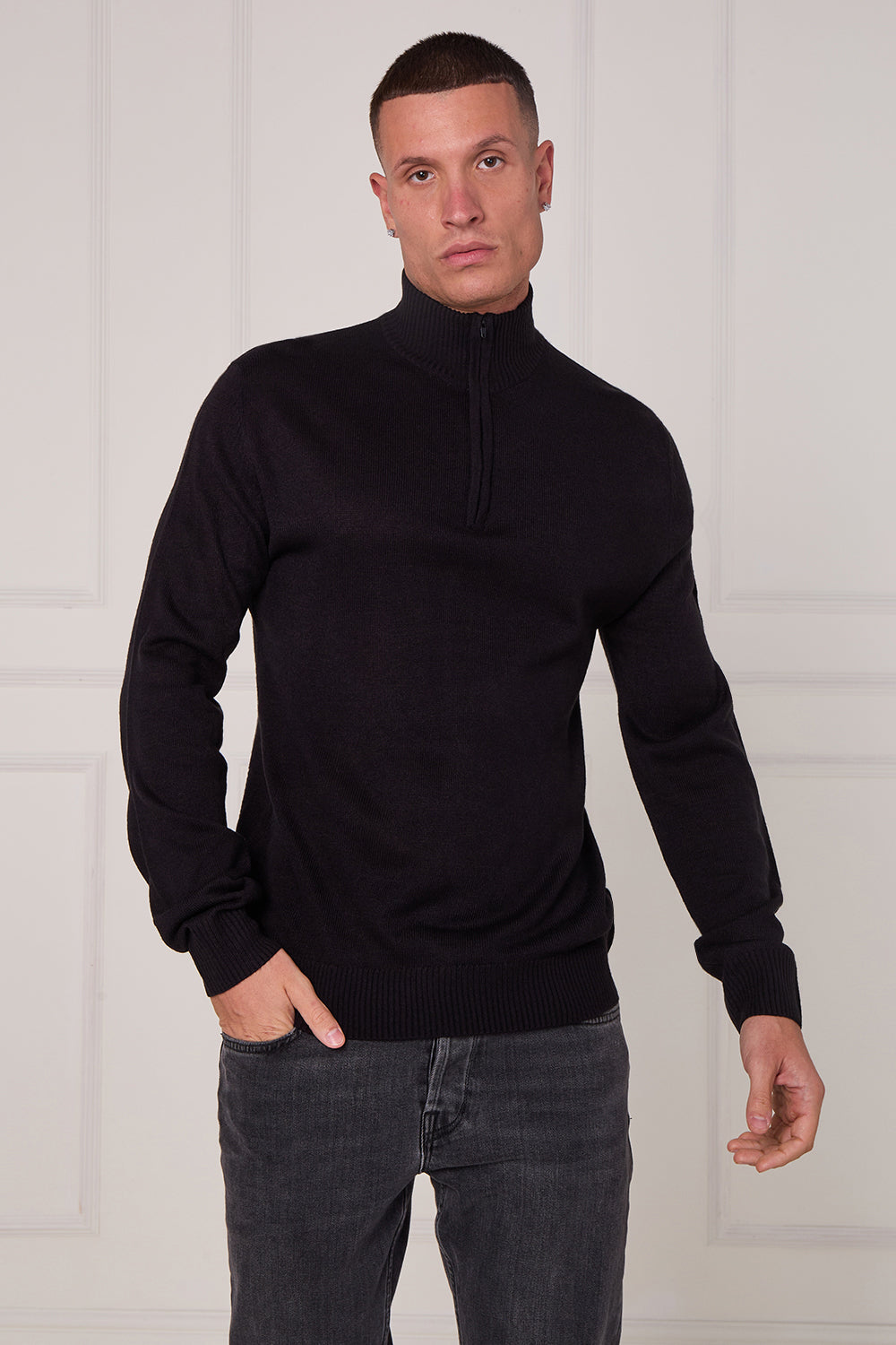 Man wearing a black turtleneck sweater and gray jeans against a white background