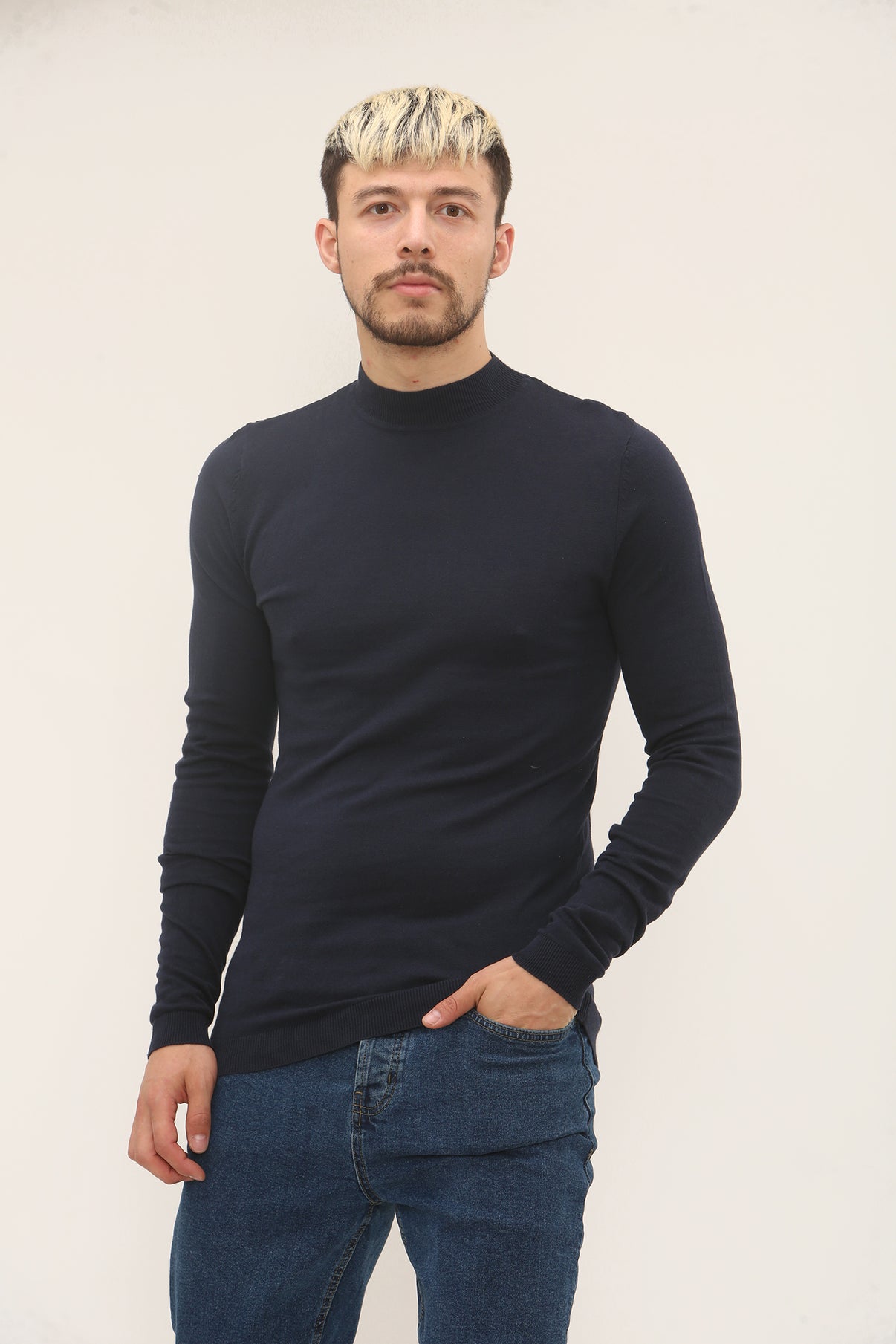 Man wearing a black turtleneck sweater and blue jeans against a plain background