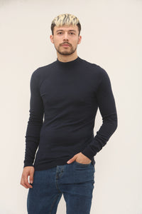 Man wearing a black turtleneck sweater and blue jeans against a plain background