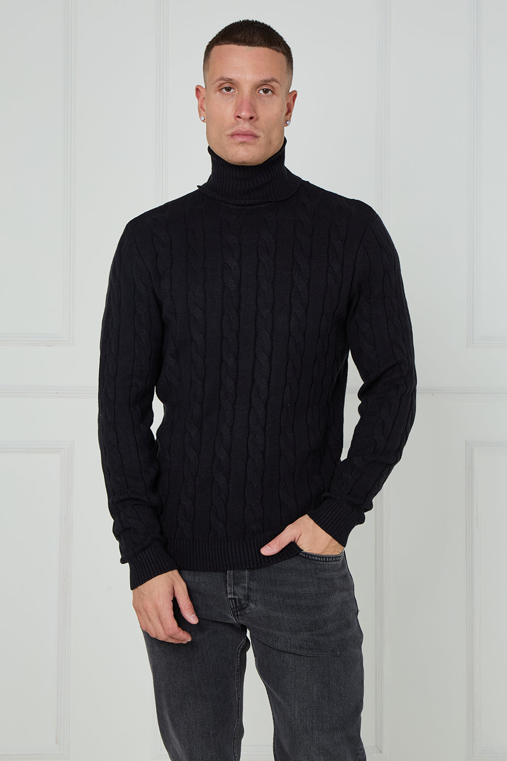 Man wearing a black cable knit turtleneck sweater against a white background