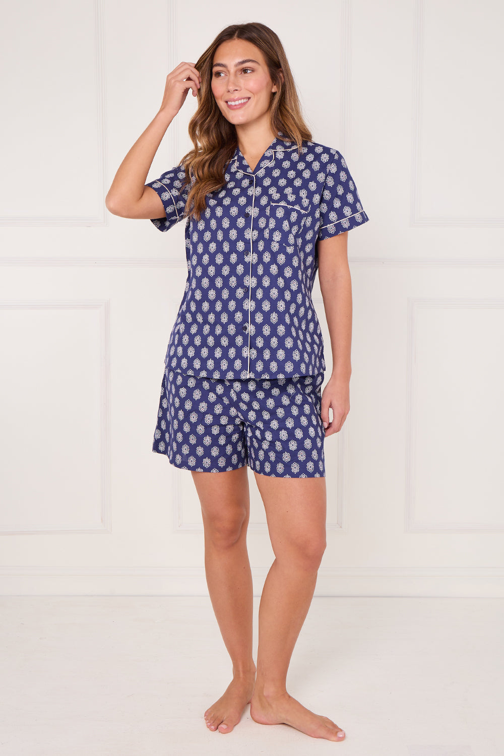 Woman wearing a navy blue pajama set with white polka dots on a white background