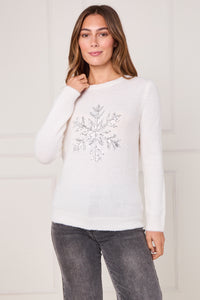 Woman wearing a white sweater with a decorative snowflake design against a plain background