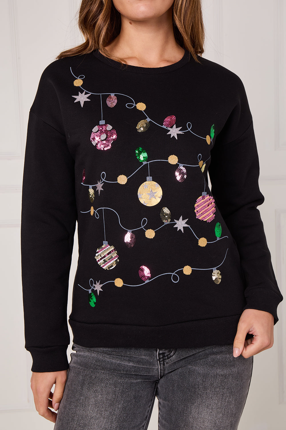 Black sweater with festive lights and ornaments design worn by a person.