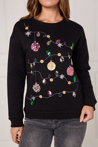 Black sweater with festive lights and ornaments design worn by a person.