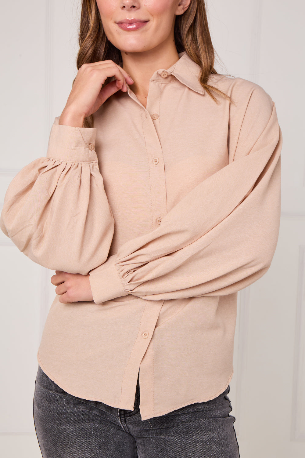 Woman wearing a beige blouse with puffed sleeves against a plain background