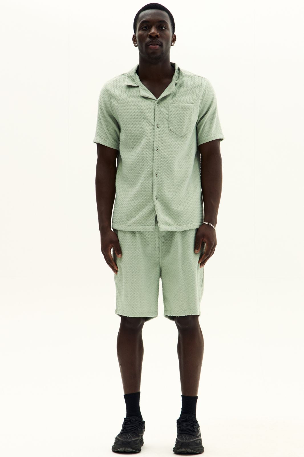 Man wearing a light green shirt and shorts set on a white background