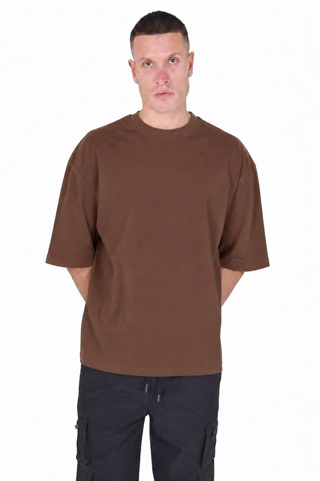 A man wearing a plain brown short-sleeve crewneck t-shirt and dark cargo pants, standing against a solid white background.