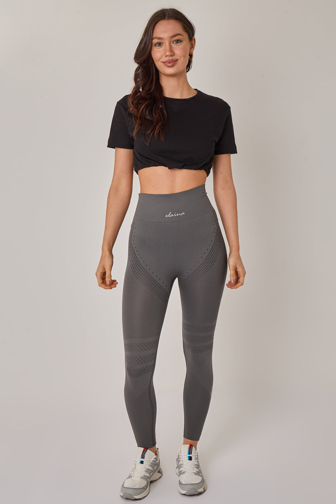 Woman wearing a black crop top and gray leggings on a plain background