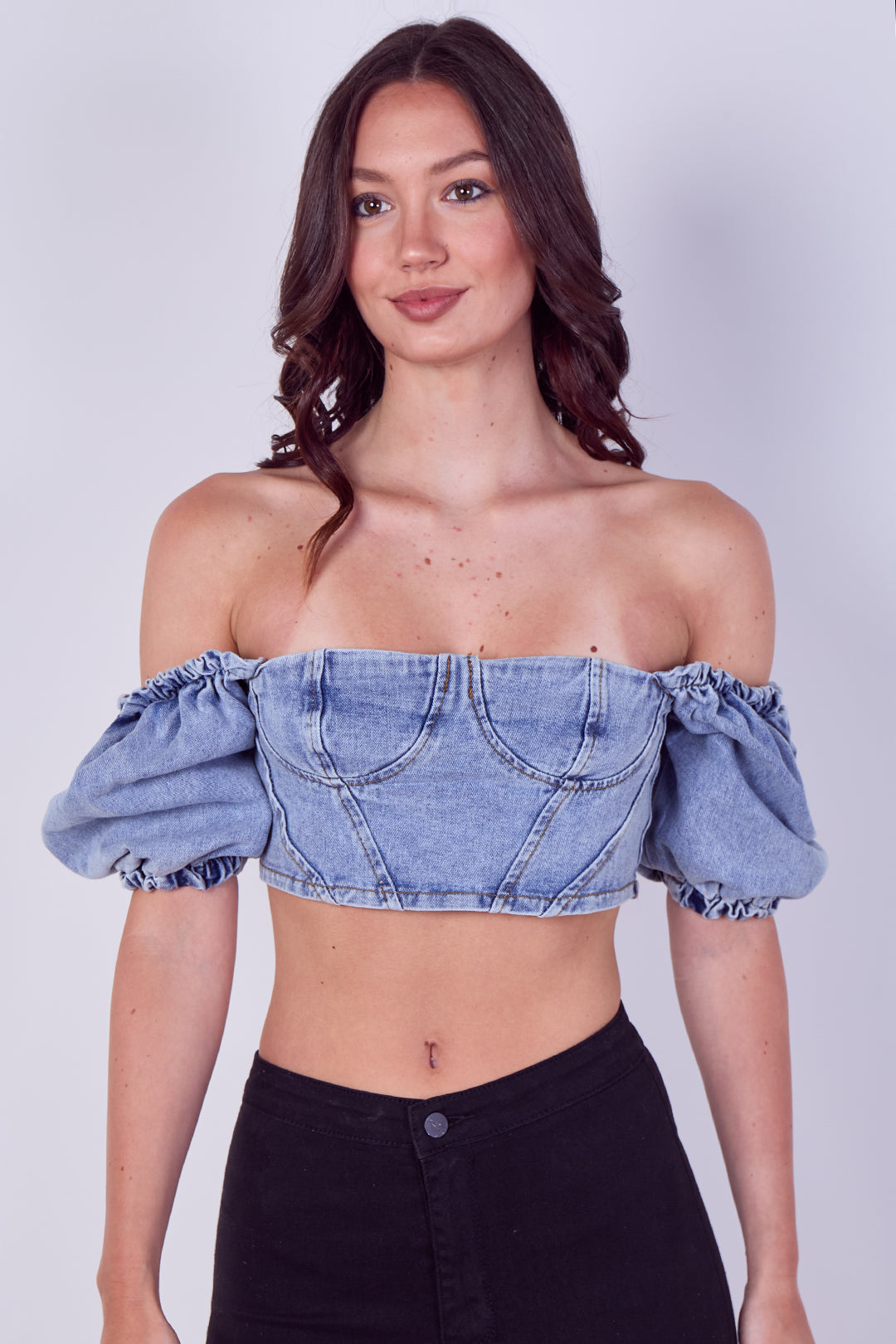 Woman wearing a denim off-shoulder top against a plain background