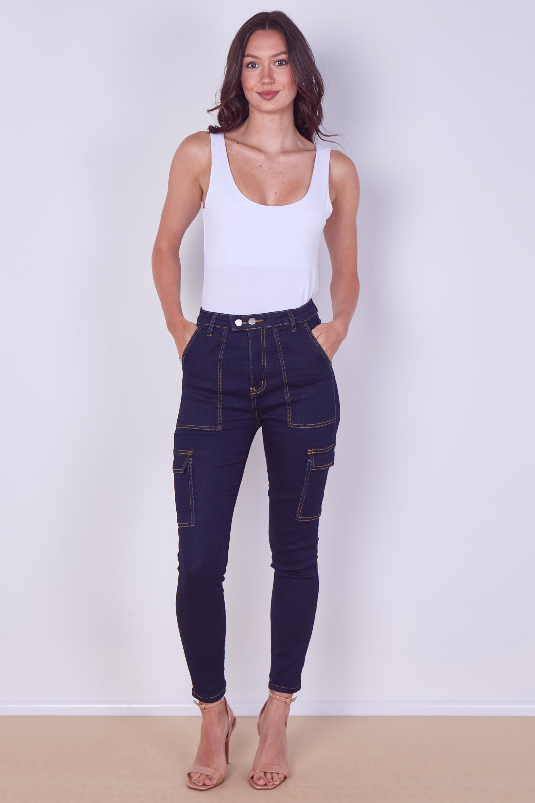 Woman wearing dark blue jeans and a white tank top against a plain background
