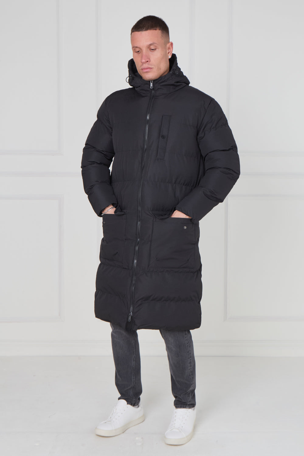 Man wearing a long black puffer coat against a white background