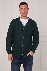 Man wearing a dark green cardigan over a white shirt with a plain background