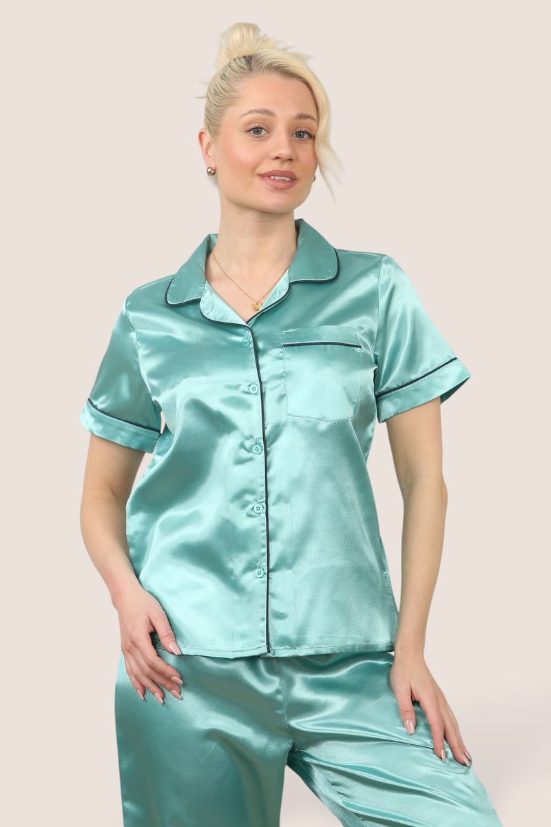 Women’s mint green satin short sleeve pajama set with button-up top and full-length pants, featuring black piping. Model is barefoot and relaxed, wearing lightweight 100% polyester sleepwear ideal for lounging and bedtime