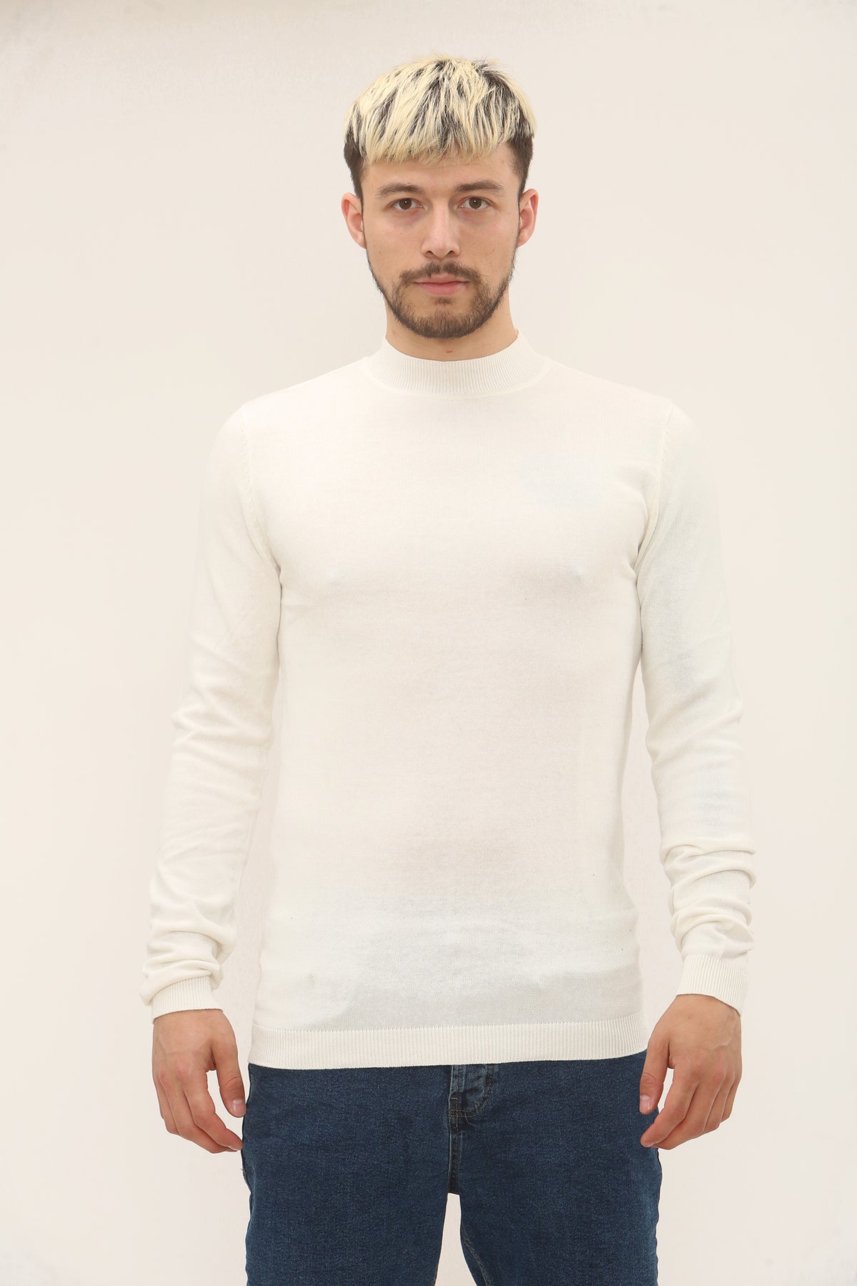 Man wearing a white sweater and blue jeans against a plain background