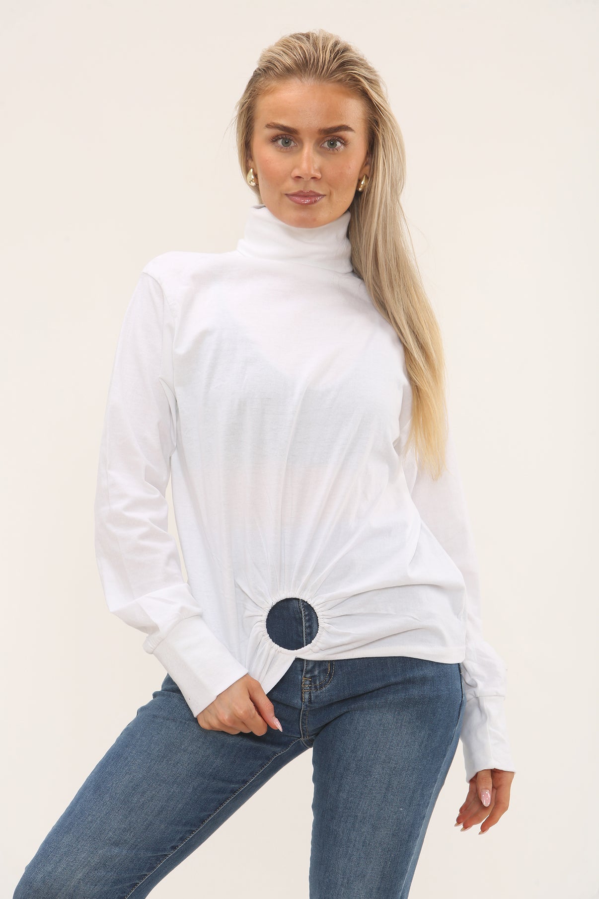 Woman wearing a white turtleneck sweater and blue jeans on a plain background