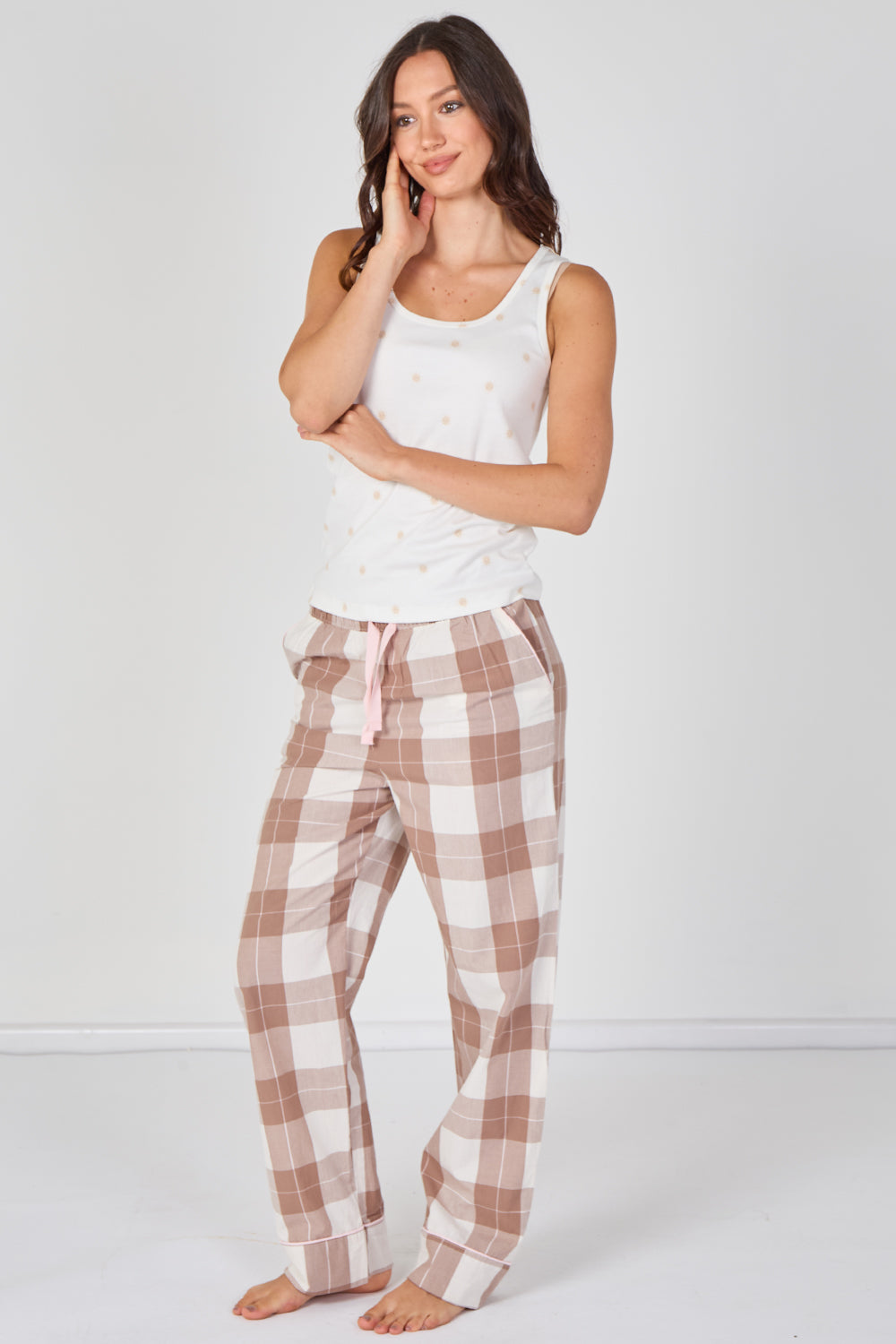 Woman wearing a white tank top and plaid pajama pants on a white background