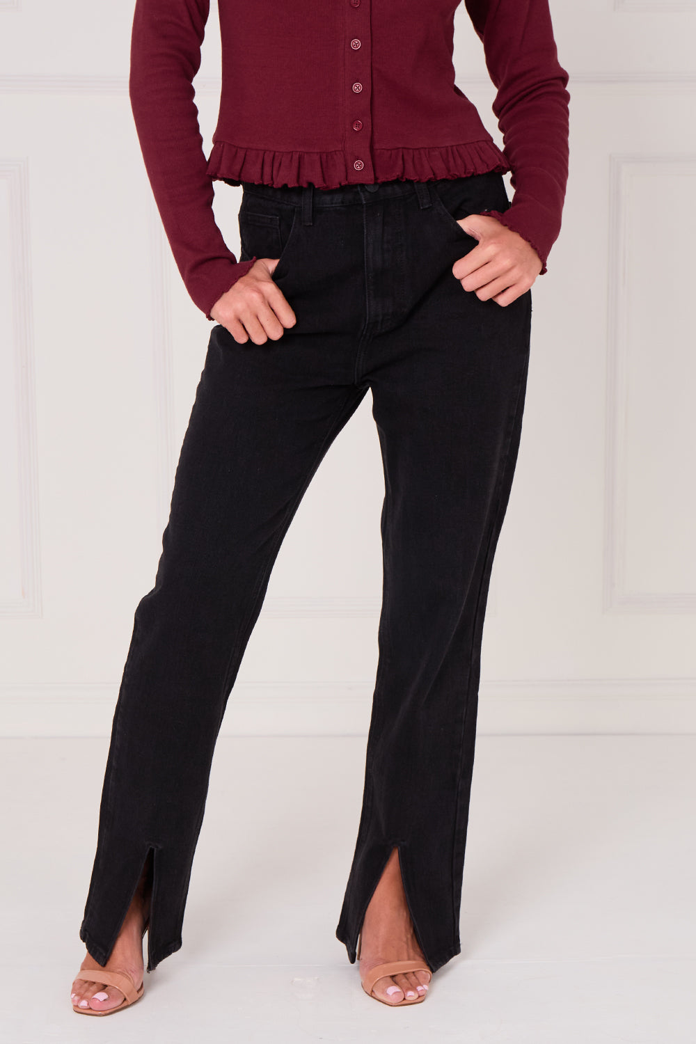 Person wearing a burgundy cardigan and black pants on a white background