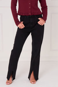 Person wearing a burgundy cardigan and black pants on a white background