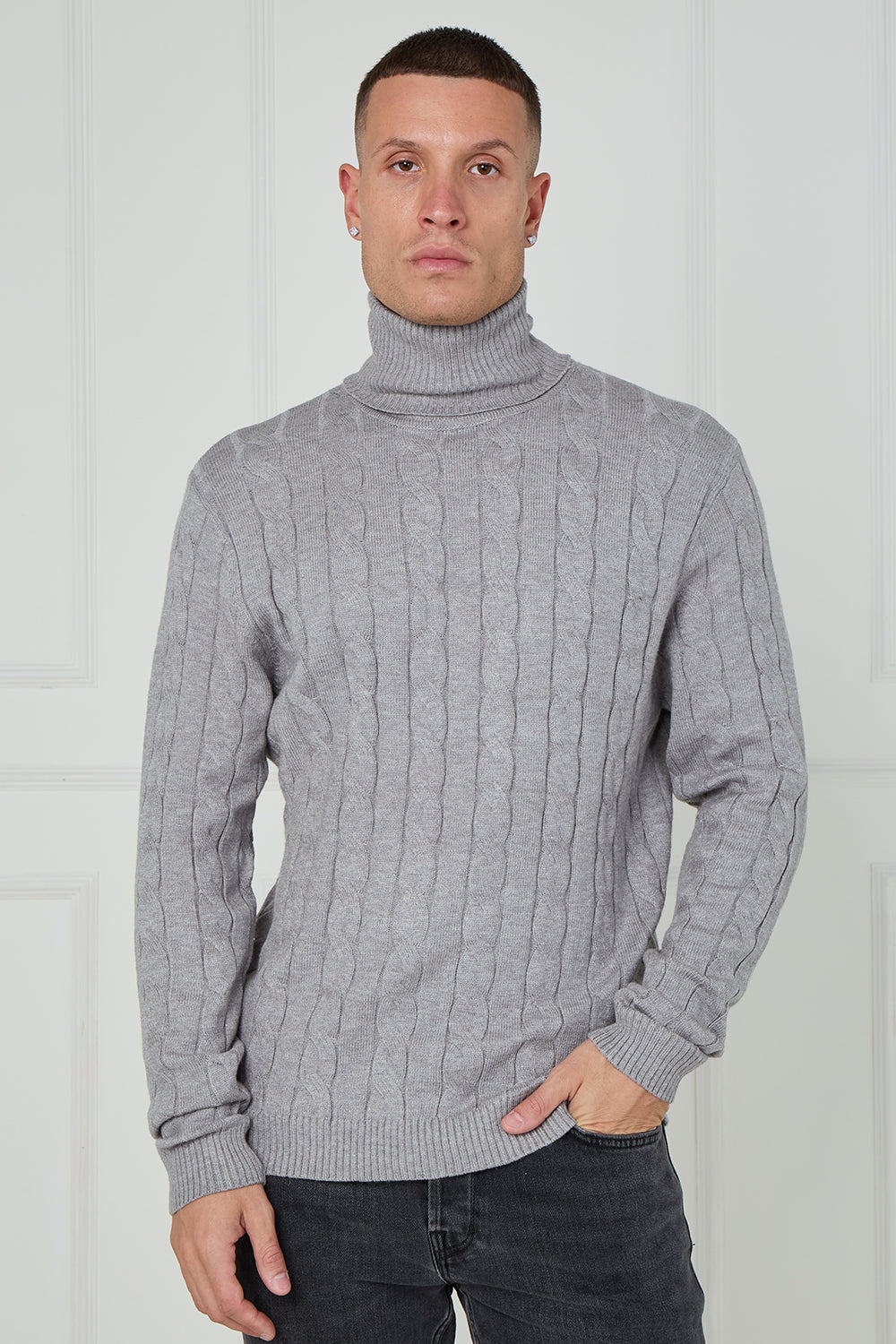 Man wearing a gray cable knit turtleneck sweater against a white background