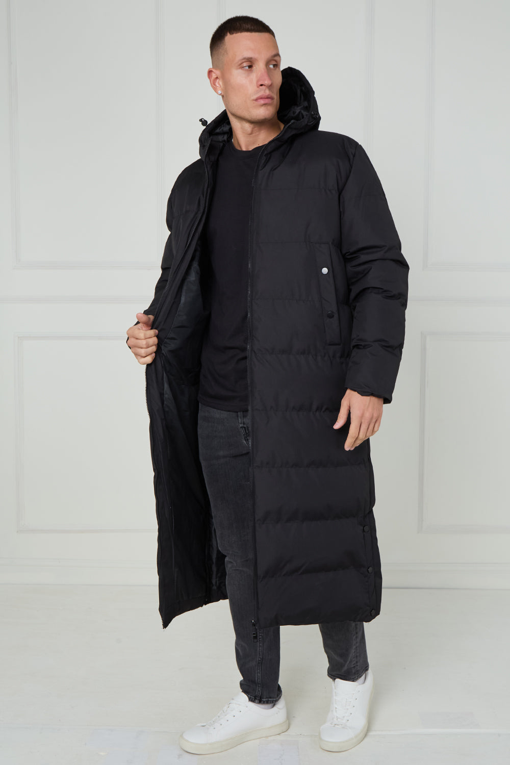 Man wearing a long black puffer coat against a white background